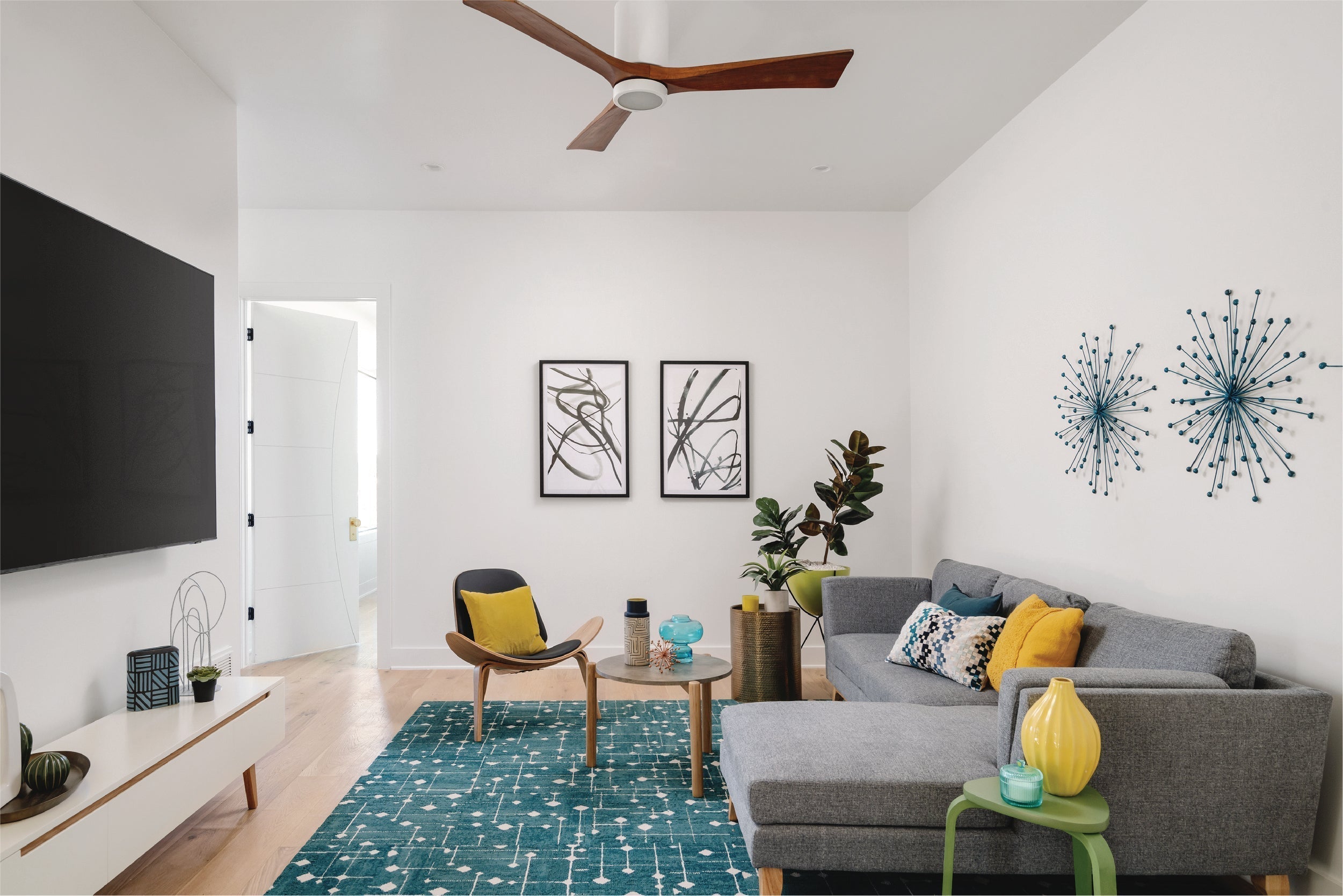 Mid century modern media room designed with grey sectional sofa, white modern tv stand, low coffee table, and modern accent chair.